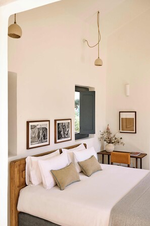 A neatly made bed with a wooden headboard, a small table with a vase of dried flowers, and framed pictures on the wall.