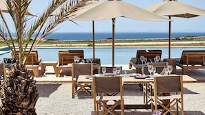 An outdoor dining area with tables and chairs, umbrellas, and a view of the ocean. - Hotel Cap Menorca - Relais & Châteaux (Alayor)