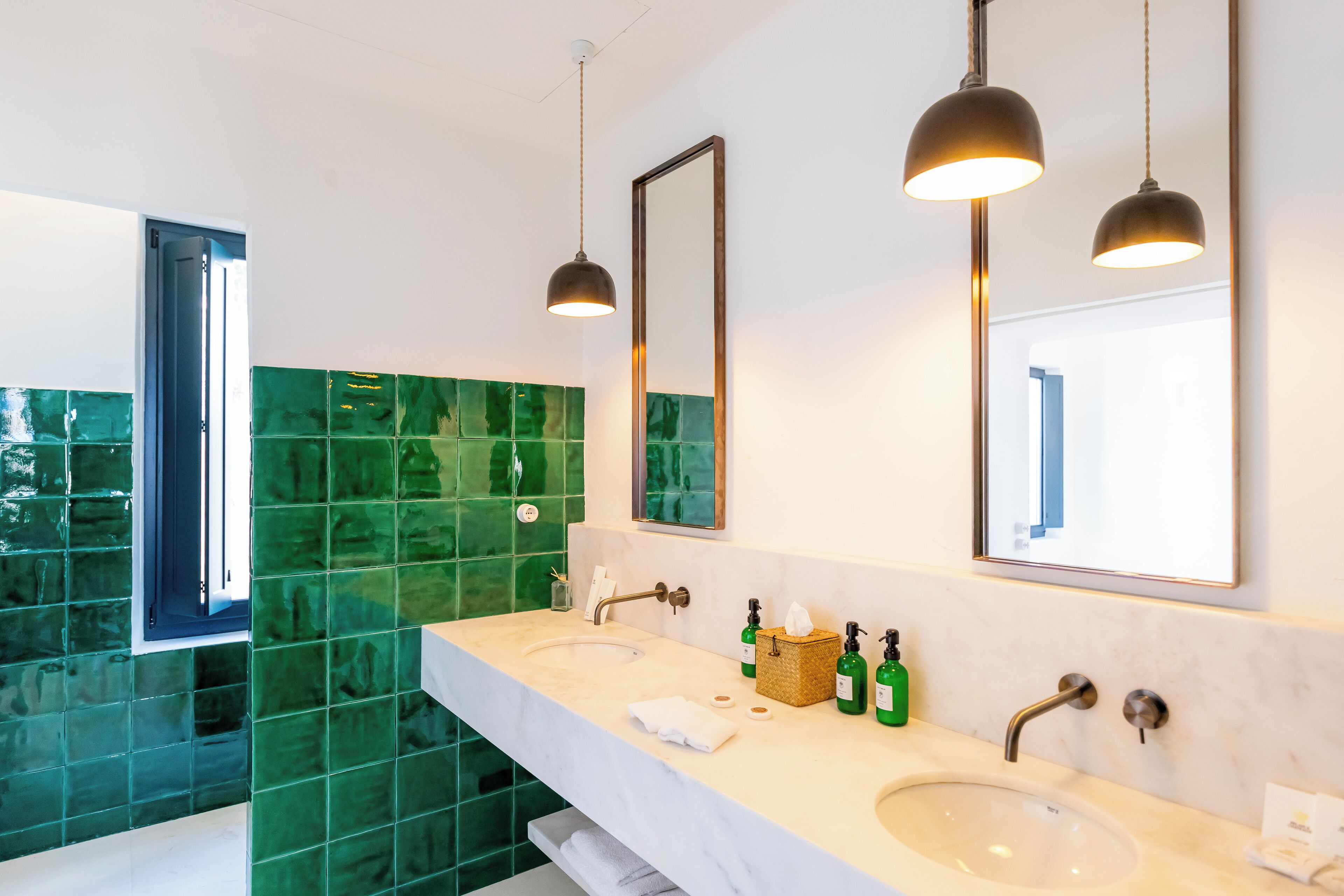 Ein modernes Badezimmer mit zwei Waschbecken, grünen Mosaikfliesen und Pendelleuchten.