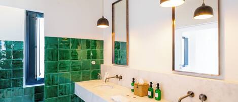 Ein modernes Badezimmer mit zwei Waschbecken, grünen Mosaikfliesen und Pendelleuchten.