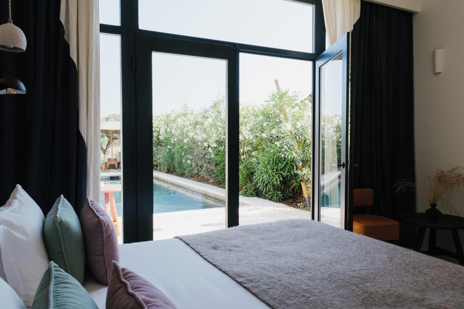 A bedroom with a large bed, a view of a swimming pool, and a sliding glass door leading to an outdoor area.