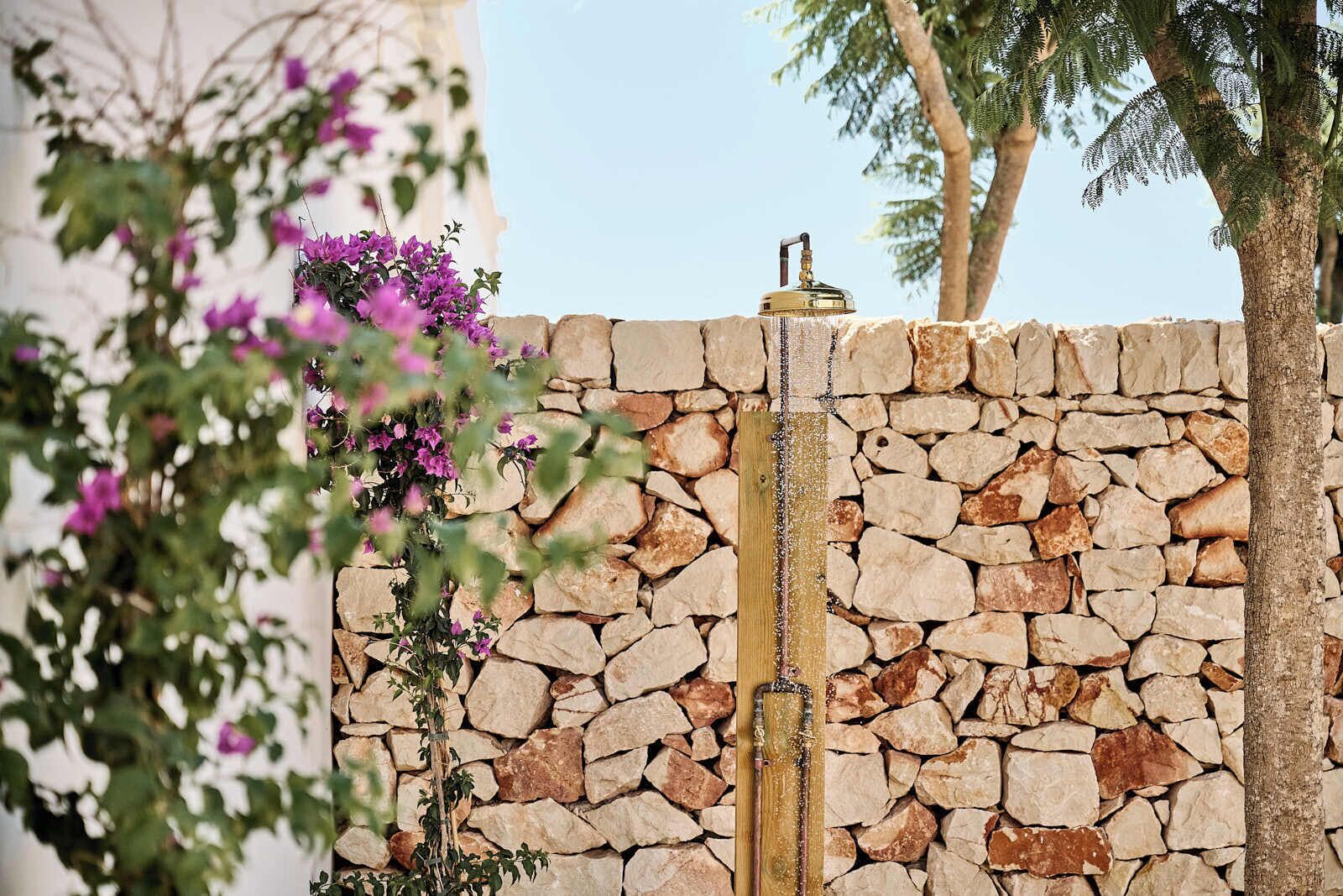 Un mur de pierre agrémenté d’un élément décoratif avec de l’eau et de plantes à fleurs.