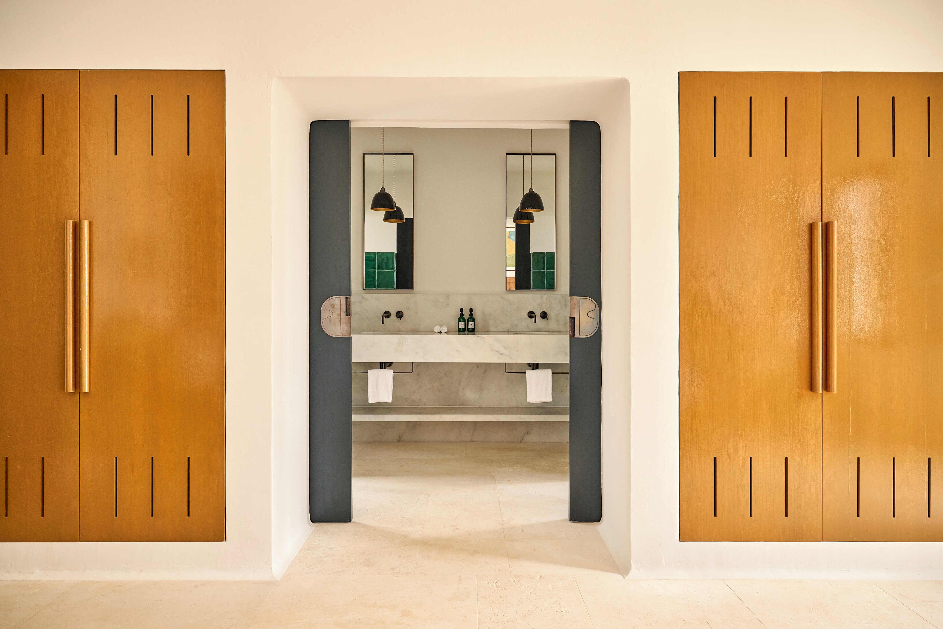 Un baño con un lavamanos central, dos espejos y armarios de madera.