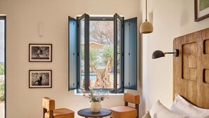A room with a bed, two chairs, a small table with a vase, and a window with open shutters. - Hotel Cap Menorca - Relais & Châteaux (Alayor)