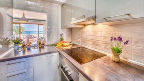 A modern kitchen with a large island, a view of the balcony, and a dining area with a view of the sea. - Blue Bay flat with swimming pool in Alcudia Beach (Alcúdia)