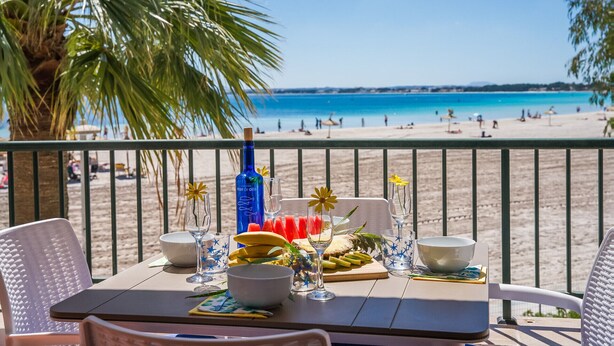 A table set with a bottle, glasses, and food on a balcony overlooking a beach. - Blue Bay flat with swimming pool in Alcudia Beach (Alcúdia)
