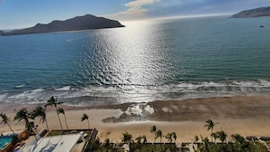 Una playa con palmeras, una piscina y vistas al océano e islas distantes.