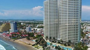 Un hotel de altura con varios balcones, una zona de piscina y vistas a la playa.