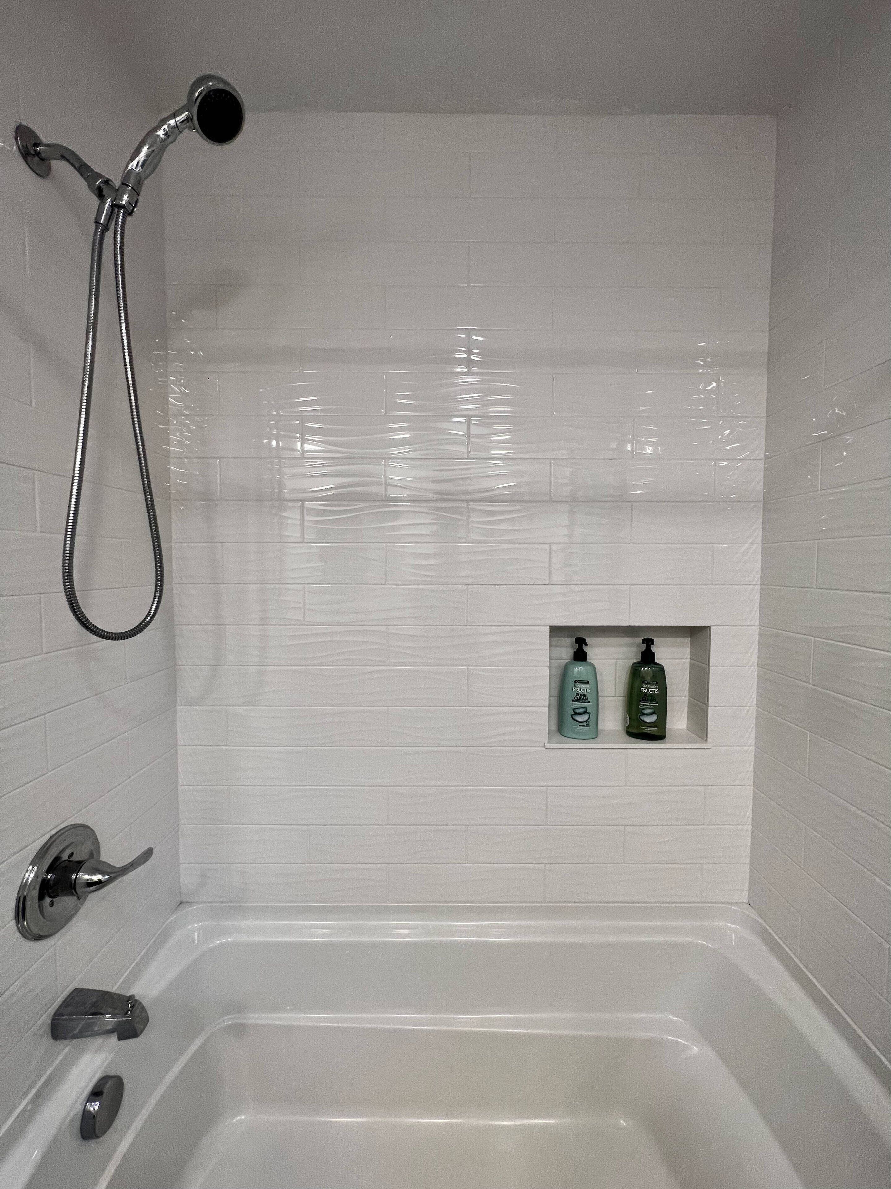 Un baño con bañera, ducha y dos botellas de champú en un estante.