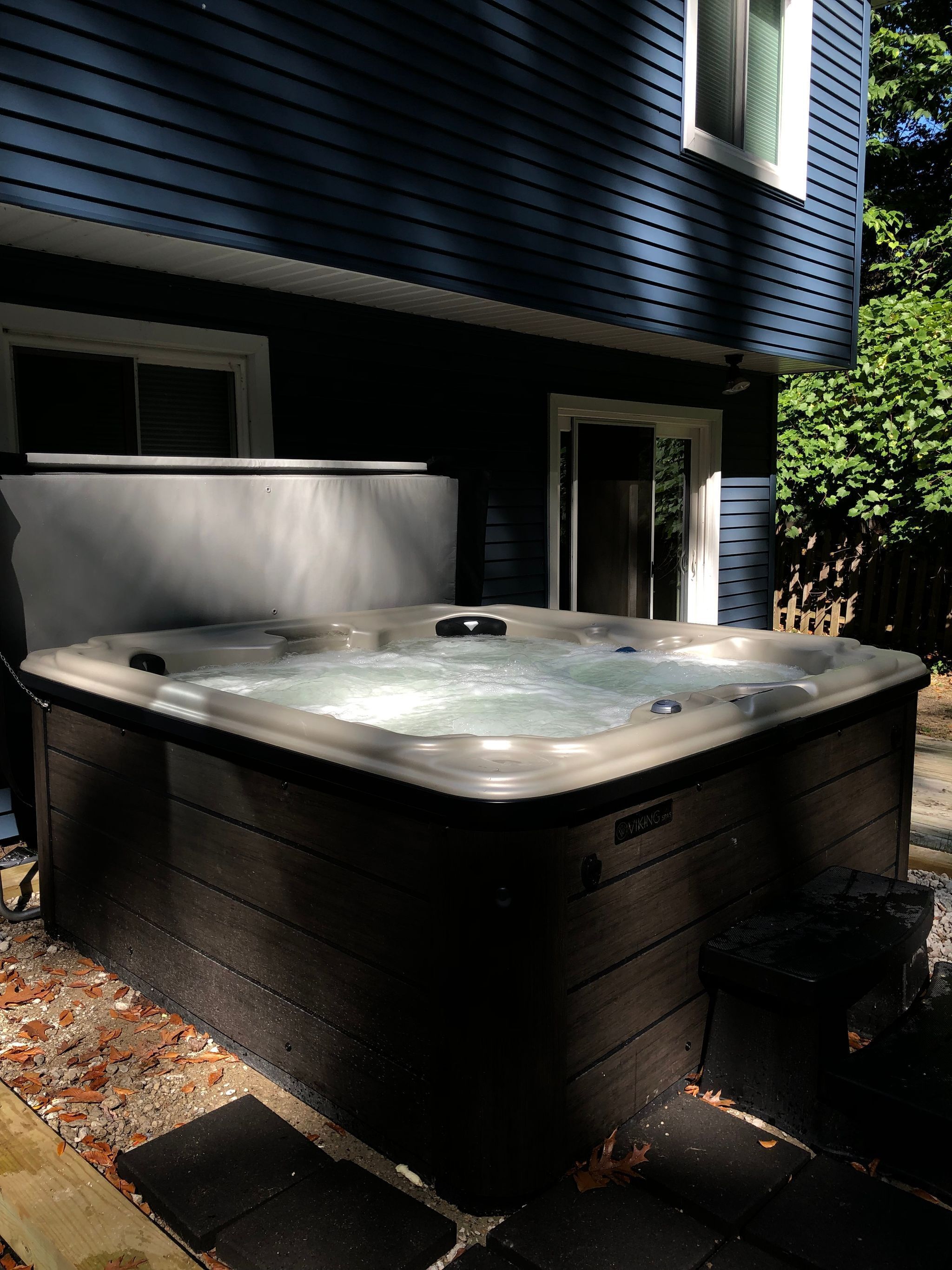 Un jacuzzi al aire libre frente a una casa de fachada oscura y un ventanal.