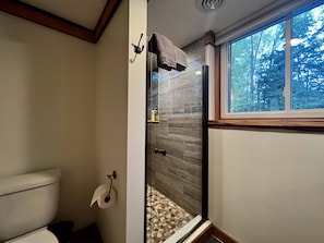 A bathroom with a glass shower enclosure, a toilet, and a window providing a view of trees. - 4BDR Long Lake Peninsula Home 7967 (Traverse City)