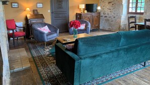 Una sala de estar acogedora con un sofá verde, dos sillones, una mesita de centro y un televisor sobre un mueble de madera.