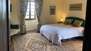 Un dormitorio con cama, una mesita de noche, una ventana con cortinas florales, un cuadro en la pared y un tapete estampado.