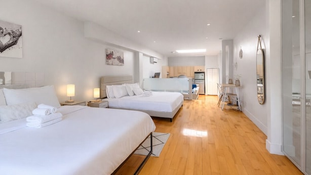 Habitació d'hotel moderna amb dos llits, una cuineta i un bany amb dutxa de vidre.