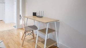 Habitació petita i moderna amb terra de fusta, un escriptori blanc amb una cadira i una petita prestatgeria.