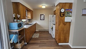 A narrow kitchen with wooden cabinets, a microwave, a refrigerator, and a clock on the wall. - Escape to a colorful, cozy retreat where families and work crews alike can relax (Fort Wayne)