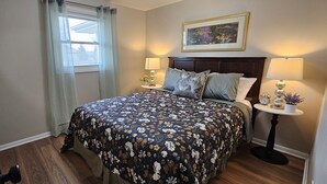 A bedroom with a floral bedspread, two bedside lamps, a nightstand with a clock, and a framed picture on the wall. - Escape to a colorful, cozy retreat where families and work crews alike can relax (Fort Wayne)