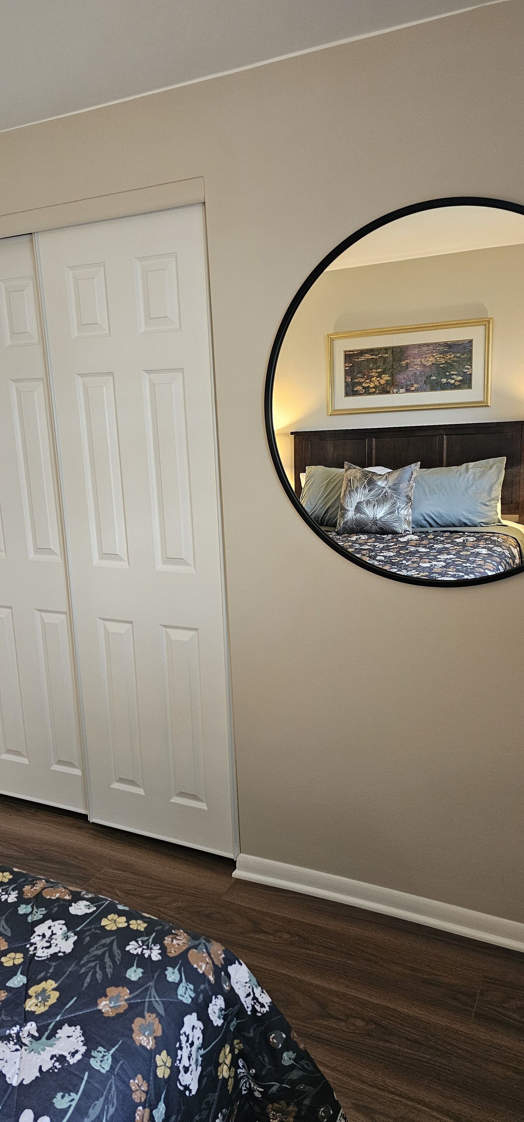 Quarto com cama, espelho redondo, porta e quadro na parede.