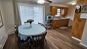 A dining area with a round table, chairs, a vase with flowers, and a window with curtains. - Escape to a colorful, cozy retreat where families and work crews alike can relax (Fort Wayne)