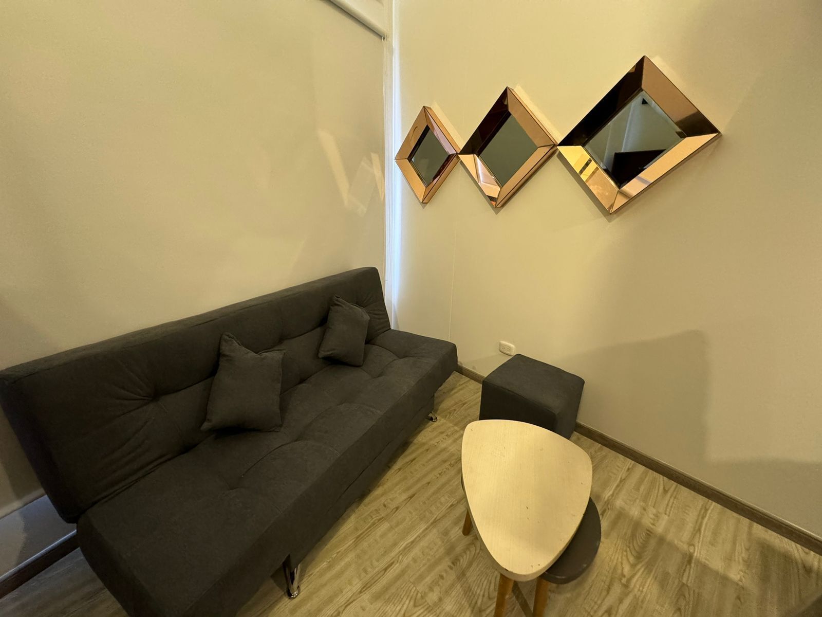 Ein modernes Wohnzimmer mit einem dunkelgrauen Sofa, einem weißen Sessel und drei an der Wand befestigten Spiegeln.