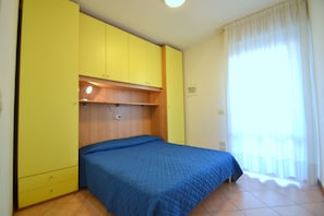A bedroom with a bed, yellow wardrobe, and a window with curtains. - Choose to Spend Your Holiday With Beahost Rentals! (San Michele al Tagliamento)