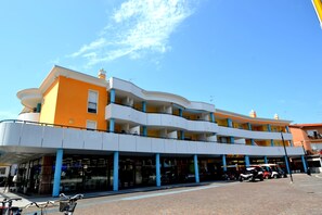 Un immeuble à plusieurs étages doté d’une façade incurvée, de balcons et d’une entrée au niveau du sol, protégée par un auvent.