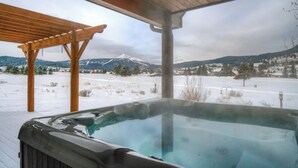 A hot tub with a wooden pergola and a snowy landscape with mountains in the background.