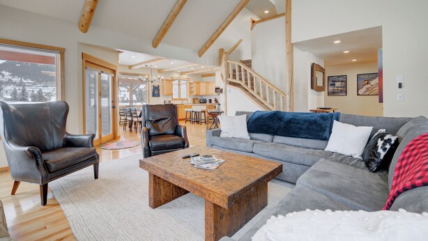 A spacious living area with a wooden coffee table, leather armchairs, and a grey sofa. A wooden staircase leads to an upper level.