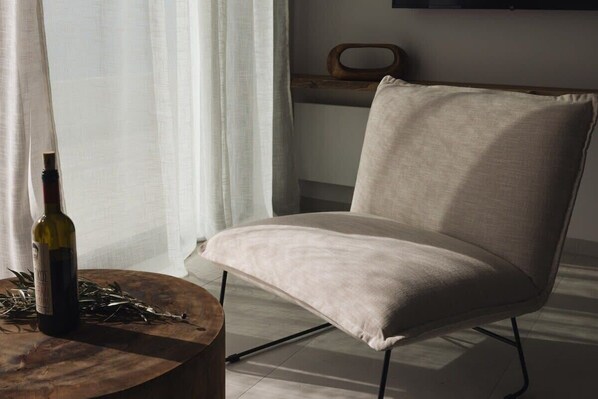A modern chair with a light fabric seat and black metal legs, placed on a wooden table beside a bottle of wine and scattered keys.
