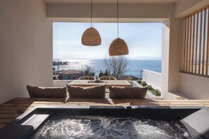 A hot tub with a view of the sea, wooden furniture, and hanging wicker lamps.