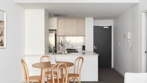 A modern kitchen with a central island, wooden chairs, and a dark door.