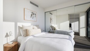 A modern bedroom with two beds, a bedside table, a lamp, and artwork on the wall.