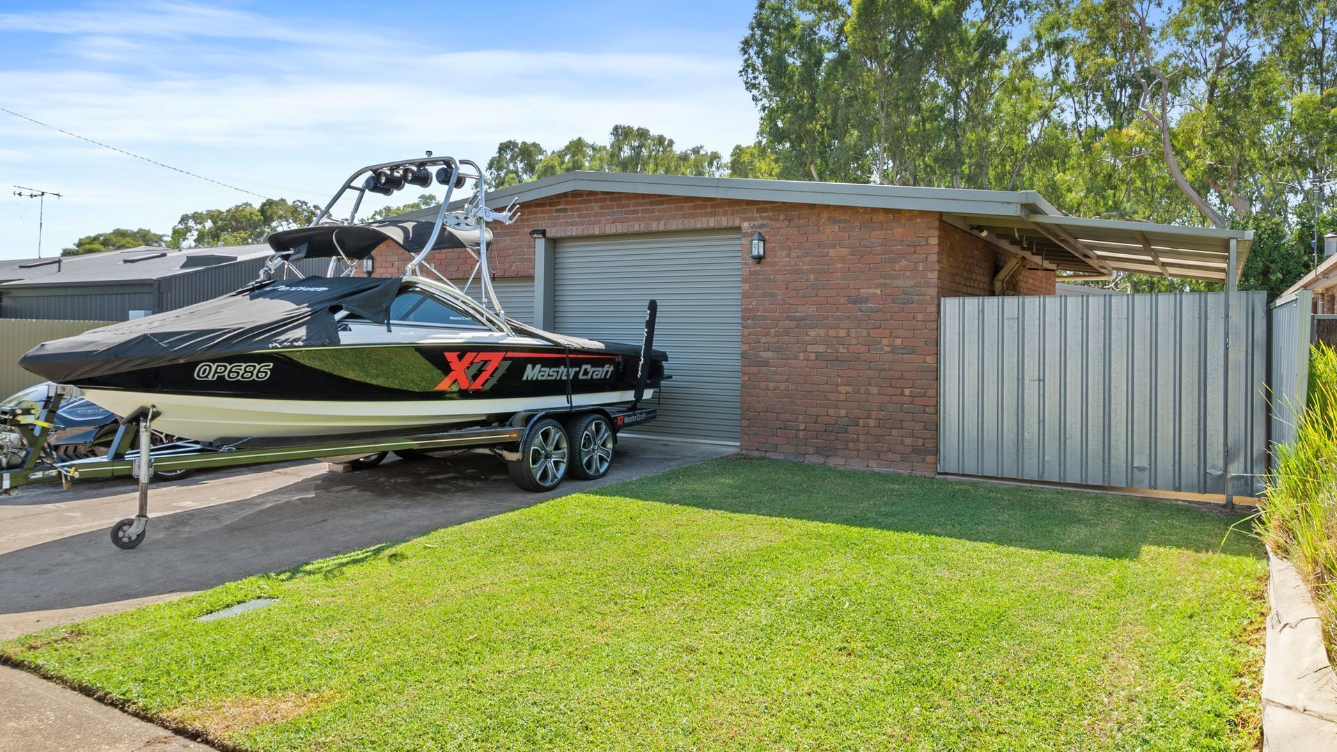 En båd ved navn 'X7 MasterCraft' med nummer 'QP686' parkeret i en indkørsel ved siden af en murstensgarage.
