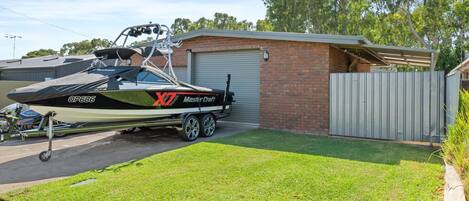 En båd ved navn 'X7 MasterCraft' med nummer 'QP686' parkeret i en indkørsel ved siden af en murstensgarage.