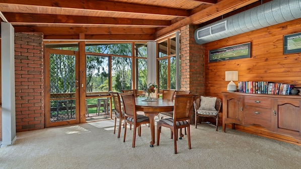 A wooden dining area with a table and chairs, a bookshelf, and a view of the outdoors. - Water's Edge Bundalong (Bundalong)