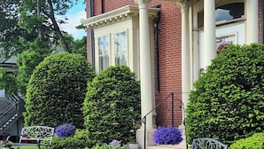 A well-maintained front yard with two benches, trimmed hedges, and a brick building with columns. - Peaceful Maine B&B Room  Cozy Stay + Farm-Fresh Breakfast Room 5 (Limerick)