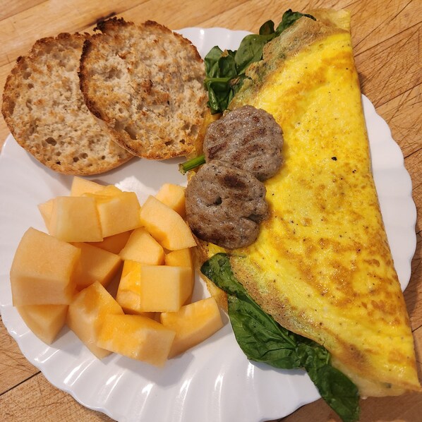 A plate with an omelette, toast, cheese cubes, and a sausage.