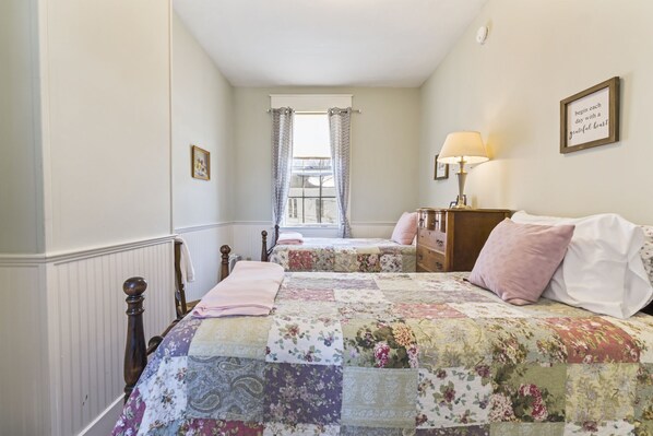 A bedroom with a large bed, a nightstand, a dresser, a window with curtains, and a view of the outside.