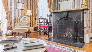 Une pièce avec une cheminée, un fauteuil, une table avec des livres et un tapis à motifs.