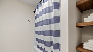 A bathroom with a striped shower curtain, a towel rack with folded towels, and a white wall. - Luxury King Studio Downtown Main Street (Hill City)