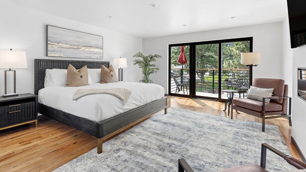 A modern bedroom with a large bed, a nightstand, a chair, and a balcony with a view. - Luxury King Studio Downtown Main Street (Hill City)