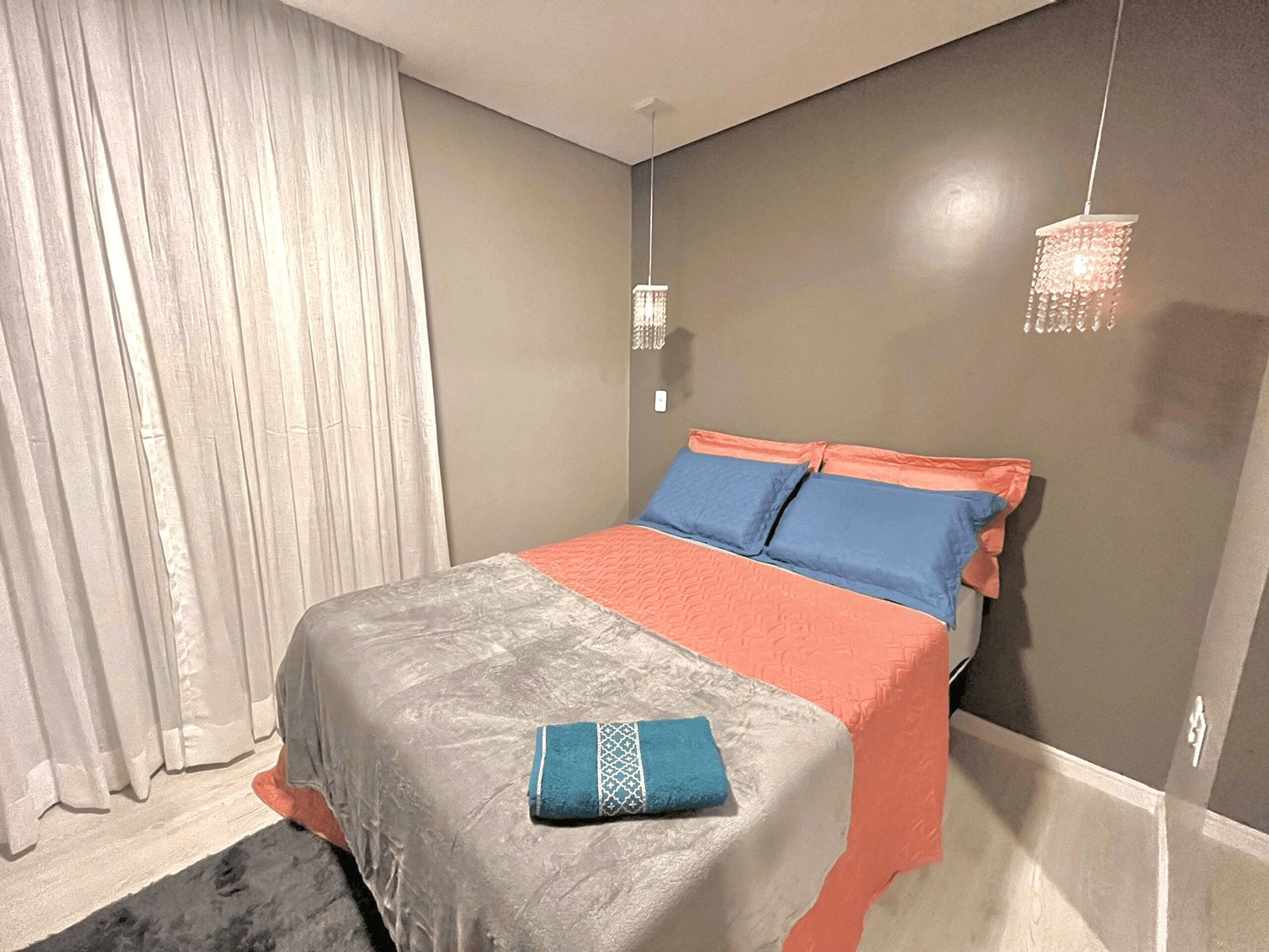 A bedroom with a bed, curtains, a hanging light fixture, and a wall-mounted light.