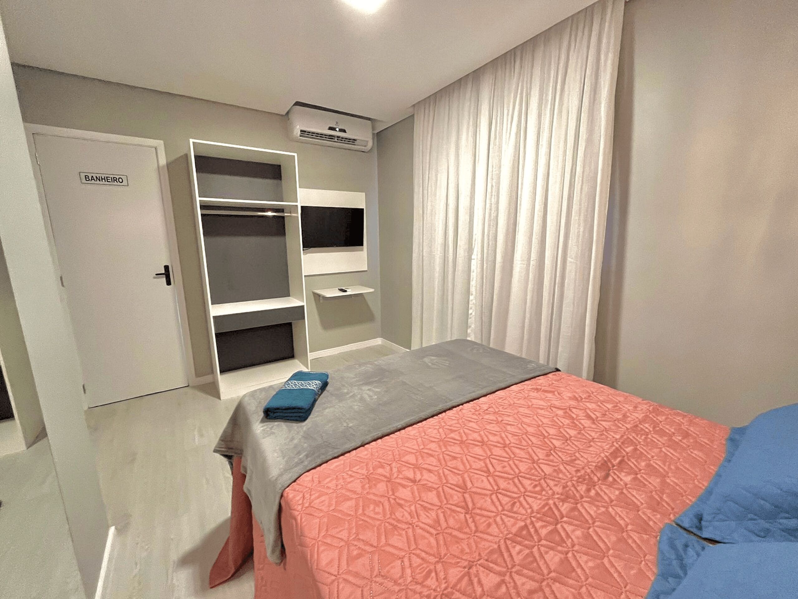 Camera da letto con un letto, un armadio, una scaffalatura e una porta con la scritta "BANHEIRO".