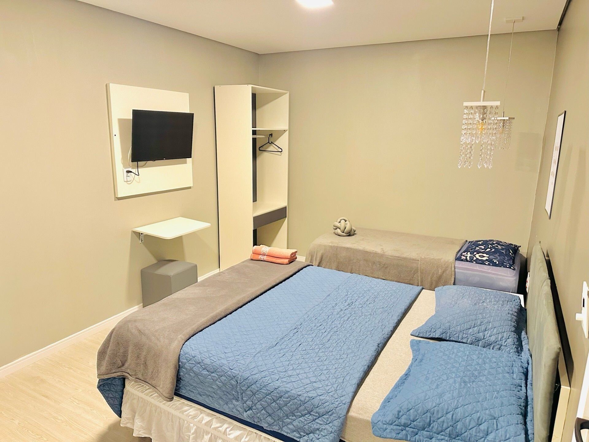 Un dormitorio con dos camas, televisor, armario y lámpara colgante.