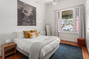 Una camera da letto con un letto, un comodino, uno specchio, una finestra con tende e un quadro appeso al muro.