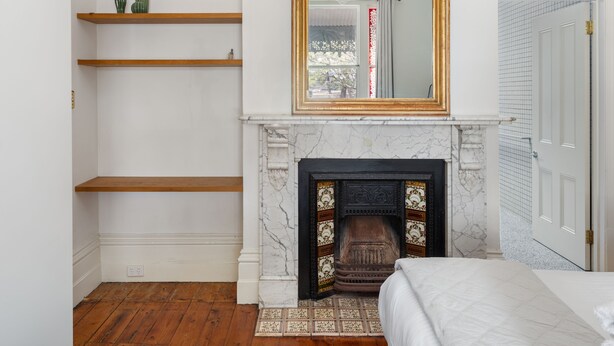 Une chambre avec une cheminée, des étagères en bois, un lit et une porte à motifs géométriques.