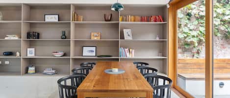 Ein Essbereich mit Holztisch und Stühlen, umgeben von Bücherregalen mit verschiedenen Gegenständen.