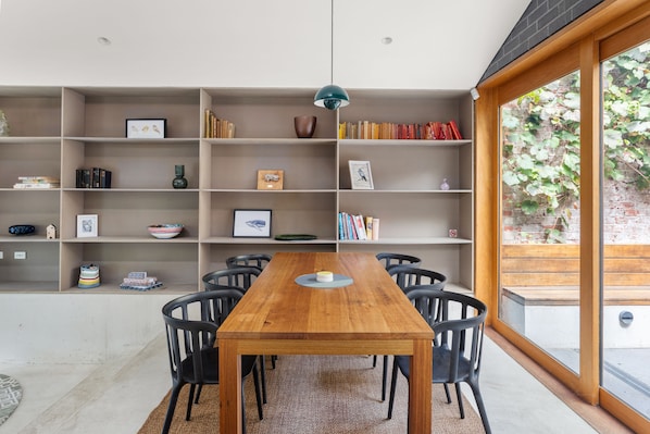 A dining area with a wooden table and chairs, surrounded by bookshelves with various items.