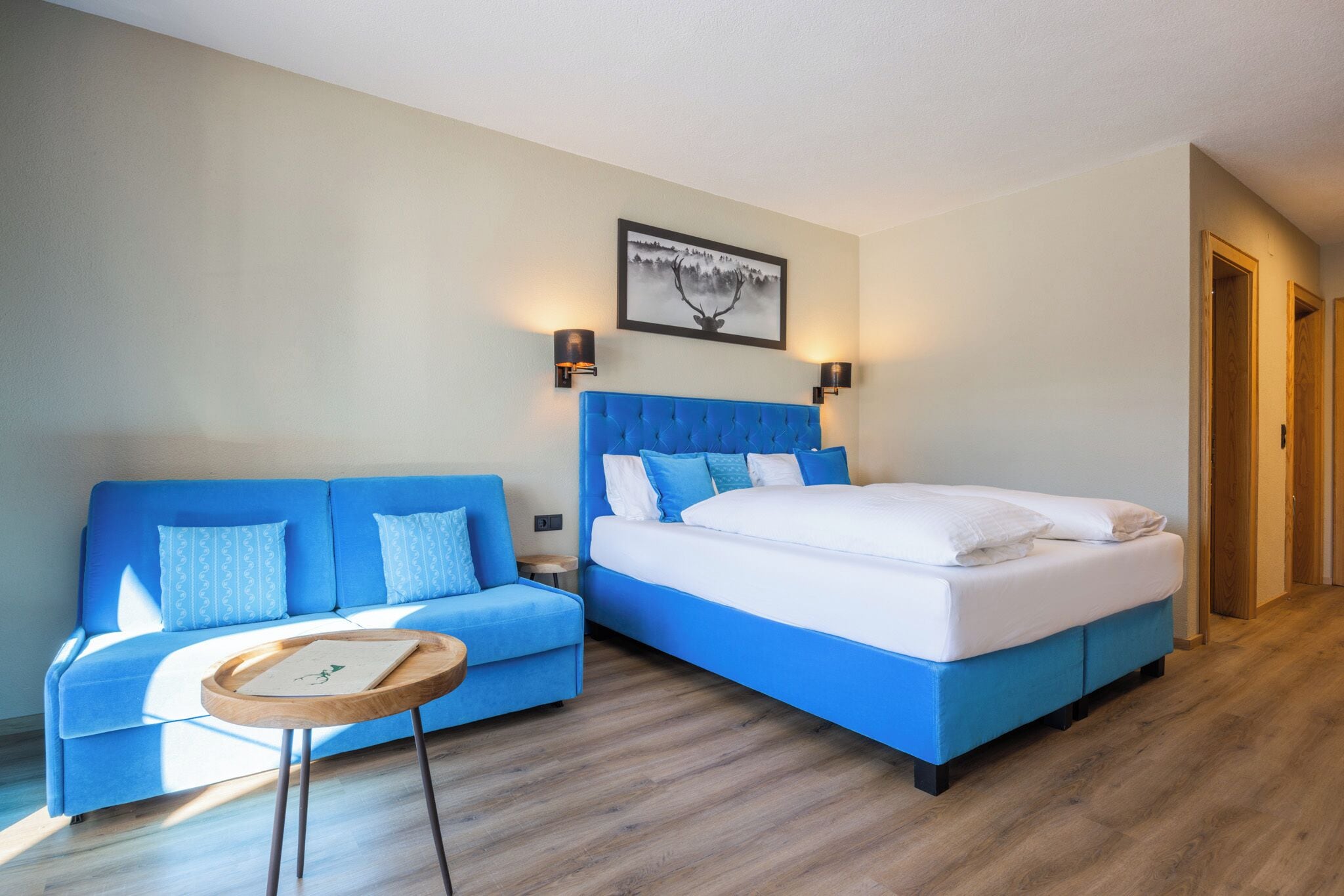 Una habitación de hotel con un sofá azul, una cama con cabecera azul y una pequeña mesita de madera.
