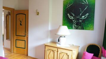 Ein Zimmer mit Holztür, einem grün gerahmten Gemälde, einer weißen Lampe und einem grünen Sessel mit rosa Kissen.